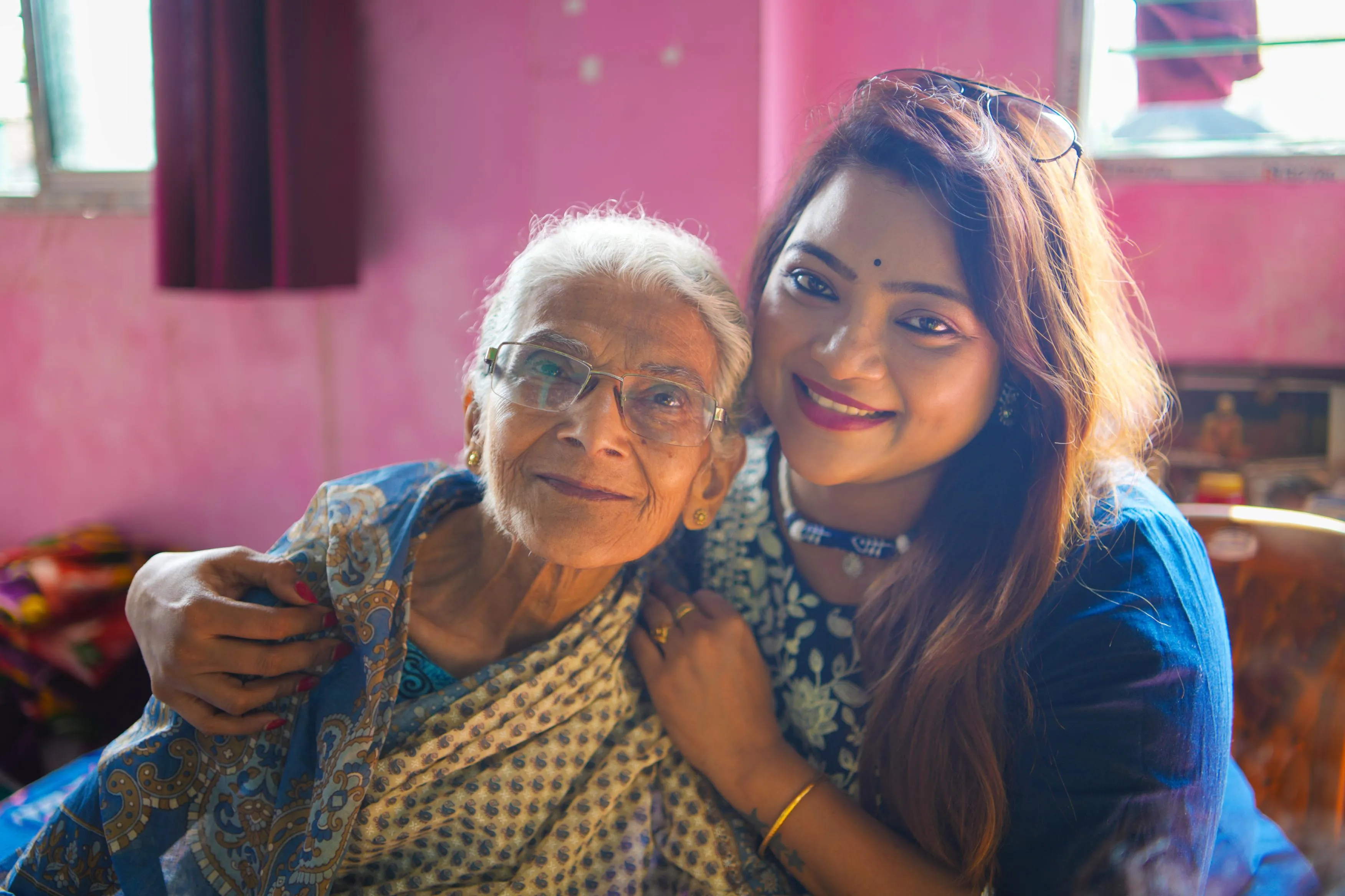 A volunteer from Nabatara Foundation – Save The Soul, the leading Elder Care NGO Kolkata, sitting beside an elderly woman in her Kolkata home, checking medicines and sharing a warm conversation while a nurse records health details in the background.